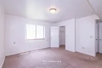 Bright and spacious bedroom in The Somerset apartment, featuring plush carpeting, large window with vertical blinds, and a walk-in closet, 2 Bed 1 Bath, 970 sq. ft.