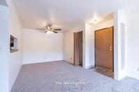 Inviting living space at The Wellington featuring plush carpet, ceiling fan, and warm wood accents, perfect for comfortable living.