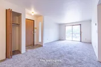 Inviting open-concept living space in The Wellington apartment featuring natural light, plush carpet, and a stylish entrance for a welcoming ambiance.