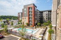 Modern apartment complex with vibrant design featuring a beautifully landscaped pool area, ample parking, and lush greenery.