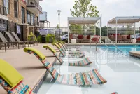 Luxurious apartment pool area featuring vibrant lounge chairs, sleek cabana seating, and lush greenery.