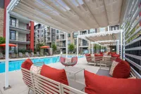 Chic apartment complex featuring a luxurious pool area with stylish seating and vibrant red cushions, perfect for relaxation and social gatherings.