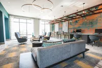Modern lounge area with stylish geometric decor, cozy seating, bold artwork, and natural light from large windows.
