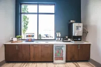 Chic refreshment corner with a sleek coffee machine, snacks, and a mini fridge stocked with beverages, set against a stylish blue wall and elegant wooden cabinetry.
