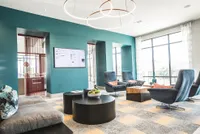Modern lounge area with stylish seating, vibrant teal accent wall, and large windows offering natural light.