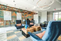 Modern lounge with stylish blue armchairs, vibrant abstract wall art, and chic wooden tables.