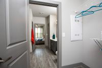 Modern apartment hallway with stylish wood flooring leading to a well-lit bedroom, featuring a sleek bathroom vanity and vibrant towel accents.