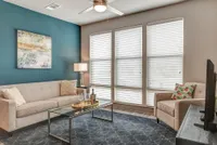 Inviting living room with elegant beige furniture, teal accent wall, and large sunlit windows, perfect for relaxation and entertaining.