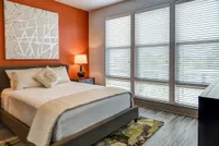 Inviting bedroom with a stylish orange accent wall, modern decor, and large windows for abundant natural light.