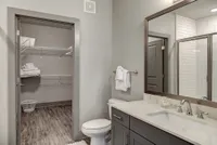 Modern bathroom with elegant gray cabinetry, a spacious vanity mirror, and a neatly organized walk-in closet.