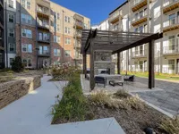 Charming apartment courtyard featuring a modern pergola with cozy seating, surrounded by lush landscaping and elegant multi-story buildings.