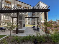 Charming apartment complex courtyard featuring a cozy outdoor seating area with a brick fireplace, elegant pergola, and lush landscaping.