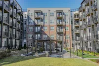 Modern apartment complex exterior with spacious balconies and a lush courtyard featuring seating and grilling areas for outdoor relaxation.