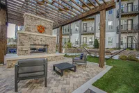 Charming outdoor lounge area with a stylish pergola, brick fireplace, and comfortable seating in a modern apartment complex courtyard.