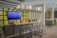 Modern communal area featuring a sleek TV wall, stylish bar seating with transparent chairs, and vibrant floral decor.