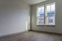 Bright, sunlit room with sleek wooden flooring and large windows offering a modern urban view.