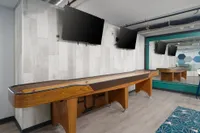 Modern entertainment room featuring a sleek shuffleboard table, dual mounted TVs, and contemporary decor.