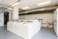 Bright and modern laundry room featuring multiple washers and dryers, with sleek industrial piping adding a contemporary touch.