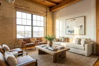 Chic loft-style living room with exposed brick, large windows, warm natural light, and stylish furnishings.