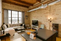 Chic urban living room with exposed brick walls, large windows, and modern decor, perfect for a cozy city lifestyle.