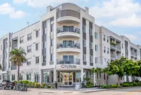 Modern apartment building exterior with sleek design, large balconies, and inviting entrance, surrounded by lush greenery.