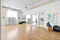 Modern fitness room with mirrored wall, wooden flooring, exercise equipment, and bright natural lighting.