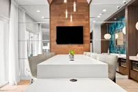 Elegant dining area with a sleek white table, modern lighting, and a warm wood accent wall with a flat-screen TV.