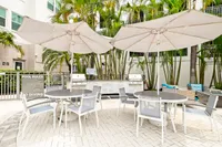 Chic outdoor patio with stylish umbrella tables, modern seating, and inviting BBQ grills surrounded by lush palm trees, perfect for social gatherings.