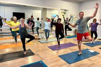 Enthusiastic yoga class enjoying a cheerful session in a bright, mirrored studio, showcasing balance and community spirit.