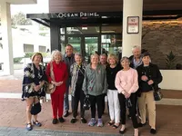 Group of smiling people posing happily in front of Ocean Prime entrance, reflecting a lively and inviting atmosphere.