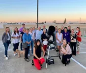 Enthusiastic group enjoying a rooftop stargazing session at sunset with a high-powered telescope.
