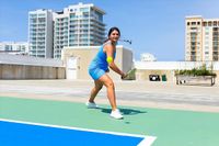 Dynamic scene of a woman enjoying pickleball on a modern rooftop court, with stylish urban apartments in the background.