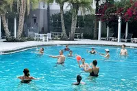 Vibrant community pool scene with people enjoying a game in crystal-clear waters, surrounded by lush palm trees and elegant loungers.