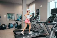 Modern gym with natural light, featuring a stylish person jogging on state-of-the-art treadmills, surrounded by elegant artwork and exercise equipment.