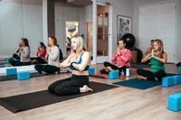 Tranquil yoga studio with women meditating on mats, surrounded by calming decor and natural light.