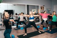 Inviting yoga studio with a mirrored wall, showcasing a group of women in a dynamic warrior pose on mats, fostering harmony and wellness.