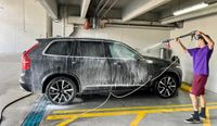 Effortless car washing in a spacious parking area, highlighting efficient cleaning with a hose and foamy lather.