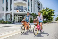 Vibrant lifestyle at CitySide apartments featuring two people joyfully biking in front of modern architecture and scenic greenery.
