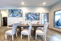 Elegant dining room with modern art, featuring a rustic wooden table and plush gray chairs, enhanced by contemporary sculptures and ambient lighting.