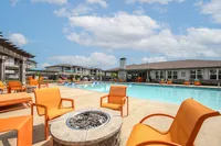 Luxurious apartment community featuring a stunning outdoor pool area with vibrant orange seating and a fire pit, perfect for relaxation under a bright blue sky.