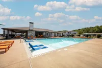 Luxurious outdoor pool area with comfortable seating, modern clubhouse, and vibrant landscape under a clear blue sky.