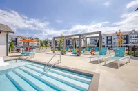 Inviting outdoor pool area featuring modern lounge chairs, vibrant umbrellas, and a stylish pergola, perfect for relaxation under a sunny sky at a contemporary apartment complex.