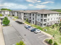 Modern apartment complex with spacious parking, surrounded by lush greenery and clear blue skies.
