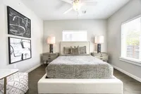 Inviting bedroom with elegant decor, featuring a plush gray bed, artistic wall paintings, and abundant natural light.