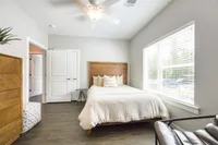 Bright and inviting bedroom with modern decor, featuring a cozy bed, natural light through large windows, and stylish wooden furniture.