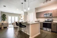 Modern open-plan kitchen and living area with sleek dark wood floors, stylish island counter, pendant lighting, and natural light flooding through large patio doors, accentuated by contemporary decor.