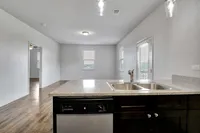 Modern apartment kitchen with sleek countertops, dual sink, and an open living space featuring hardwood floors and abundant natural light.