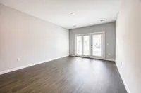 Bright, open living space with elegant hardwood flooring and double French doors leading to a sunlit patio.