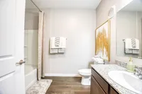 Elegant bathroom with modern design featuring granite countertop, wooden cabinetry, and stylish wall art. Bright and inviting space with a shower-tub combination and plush towels.