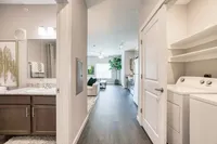 Inviting apartment hallway with dark wood flooring, showcasing a modern bathroom, cozy living area, and in-unit laundry.